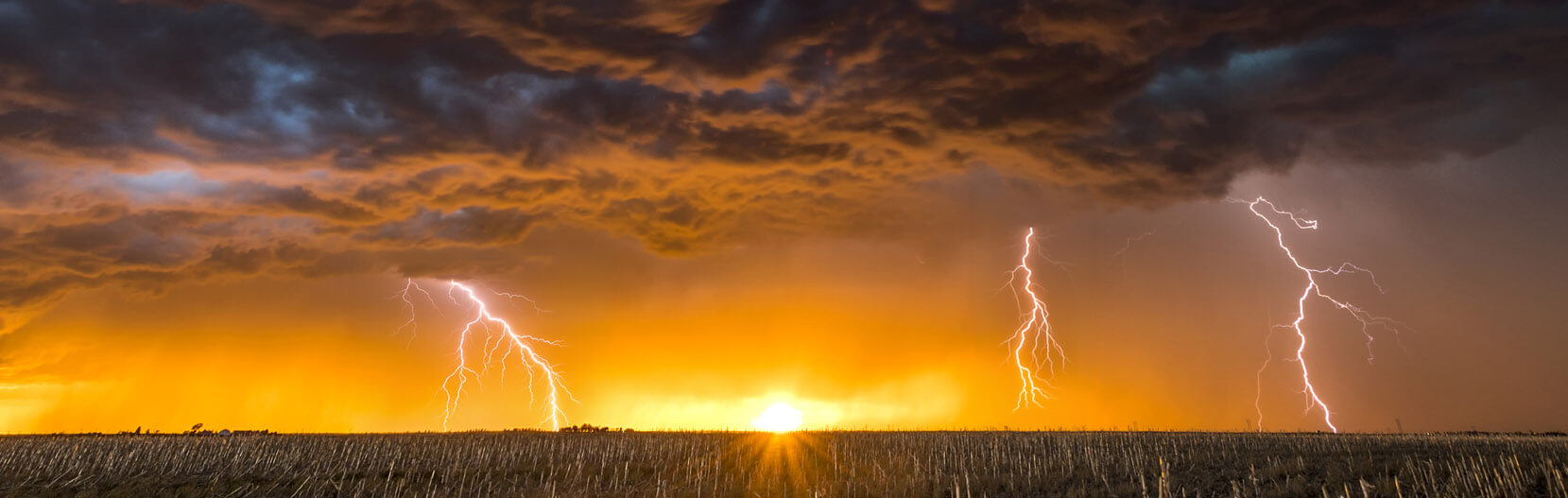 A sunset over a field with dark clouds and lightning. A metaphor for cloud security threats
